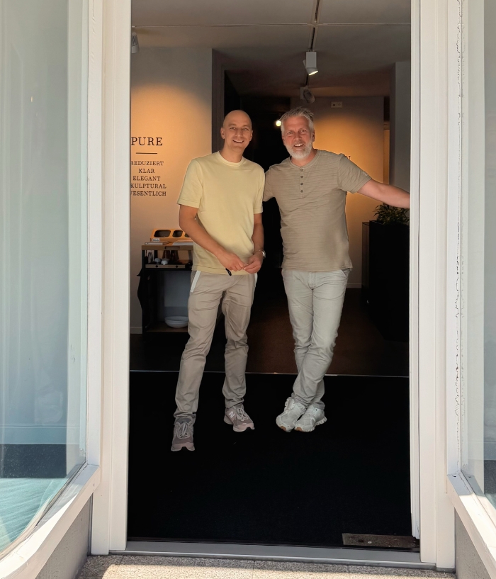 Zwei lächelnde Männer und Küchenberater im Eingangsbereich eines modernen Küchenstudio in Olpe