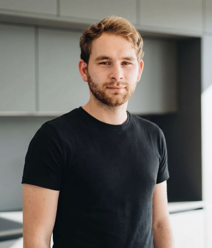 Yannik Ande — Porträt eines jungen Mannes und Küchenmonteurs vor dunklen Küchenschränken